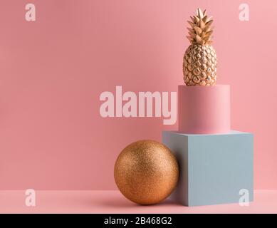 Golden pineapple, teal cube and pink round box on pink background Stock Photo