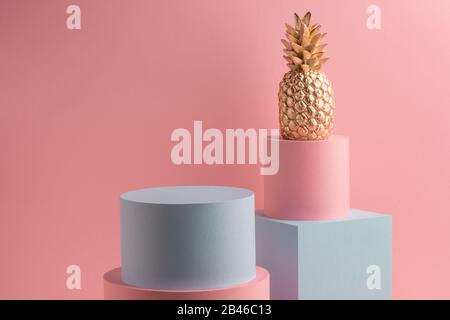 Golden pineapple, teal cube and pink round box on pink background Stock Photo