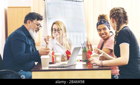 Multi-ethnic employees group enjoy takeaway food friendly conversation in office Stock Photo