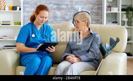 Female nuse helping senior elderly retired woman how to use her tablet computer in nursing home Stock Photo