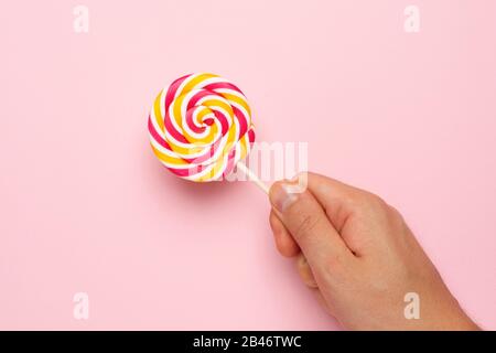 Colorful lolipop in hand , pink, yellow and white spiral on pink background , childhood sweets top view Stock Photo