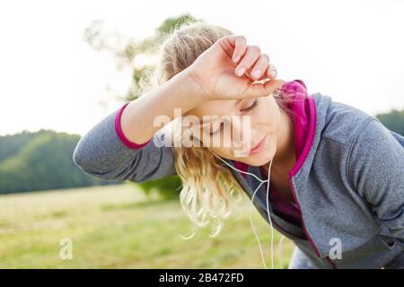 Exhausted woman wipes sweat from her forehead while jogging Stock Photo
