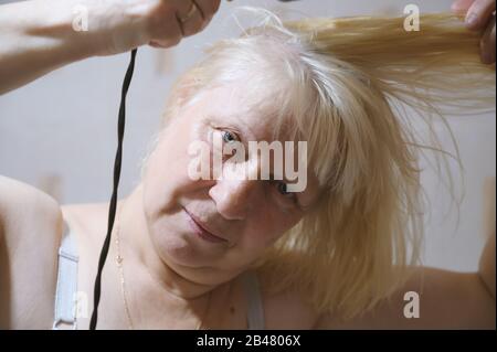 Aged woman dries hair with a hairdryer at home. Stock Photo