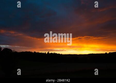 Spectacular fiery orange sunset over rolling hills silhouetted against the colorful cloudy sky in a weather or beauty in nature concept Stock Photo