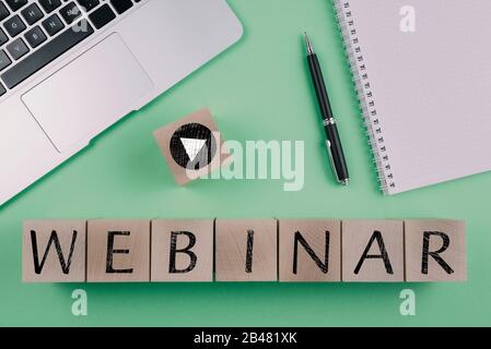 word WEBINAR and play button symbol on wood cubes against green background with laptop and notepad, e-learning and education concept Stock Photo
