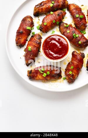 Close up of bacon wrapped grilled chicken wings on plate over white stone background with free space. Tasty snack from chicken meat, bacon in sweet, s Stock Photo