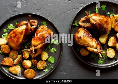 Tasty grilled quails with baked potato wedges on black stone background. Roasted quails on plate. Top view, flat lay, close up Stock Photo