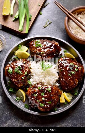 Sweet and spicy honey grilled chicken thighs with rice over dark stone table. Tasty food in asian style. Stock Photo