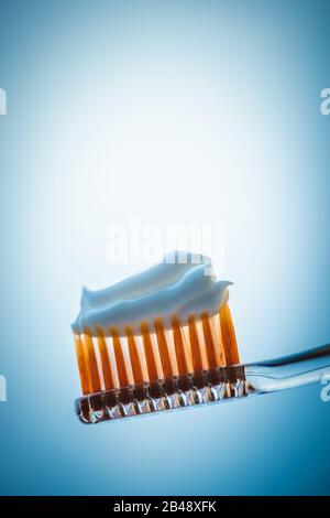 Plastic toothbrush with white toothpaste on a blue background. Stock Photo