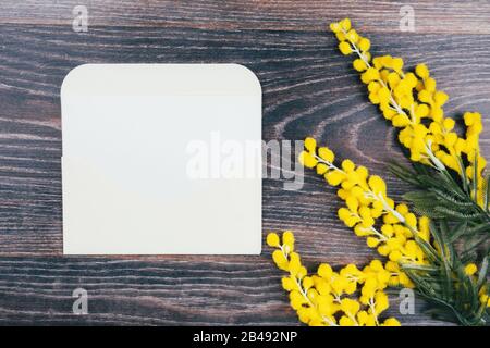 Mimosa branches and an envelope with a note on a dark wooden background Stock Photo