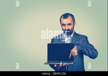 Closeup portrait of mature middle age business man showing pointing presenting a laptop screen or button with index finger. Portrait of Mixed race bea Stock Photo