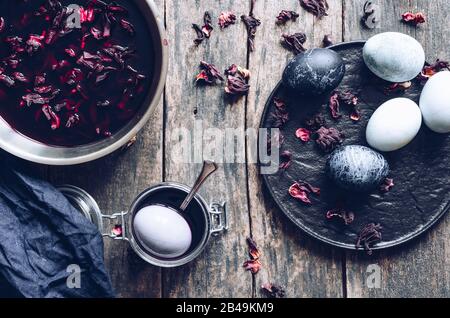 Dyed Easter eggs with marble stone effect painted with natural dye carcade tea from hibiscus flowers on old wooden background. Process of dyeing eggs Stock Photo
