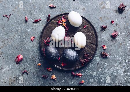 Dyed Easter eggs with marble stone effect painted with natural dye carcade tea from hibiscus flowers on dark blue concrete background. Top view. Stock Photo