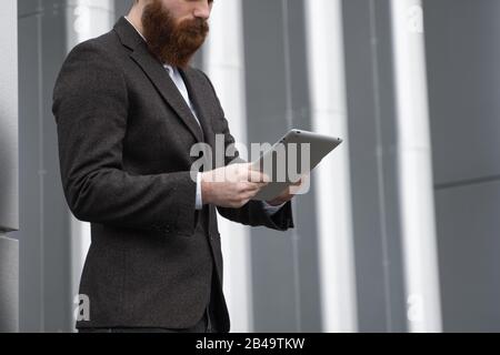 Modern Young bearded Business man working with a digital tablet. Young hipster businessman holding tablet in hands outdoor. Working online with a Stock Photo