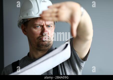 Man wearing hard hat hold in hands blueprint controlling construction site Stock Photo