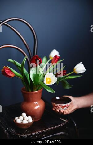 Man holding ethnic bowl with tea near beautiful bouquet of tulips and kurt balls dry cheese on wooden vintage chair at Nauryz festival Stock Photo