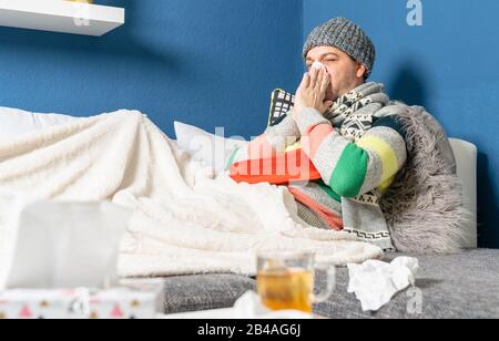 a man suffering from flu lies on the couch in the living room Stock Photo