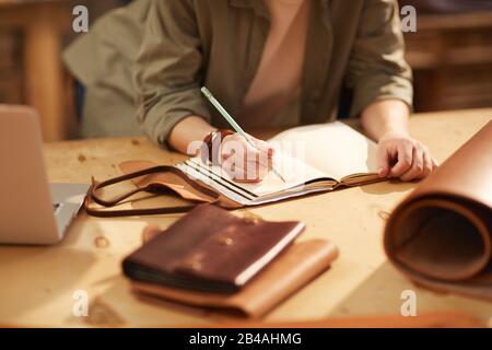 Horizontal shot of unrecognizable woman wearing casual clothes sitting at table making notes in handmade notebook Stock Photo