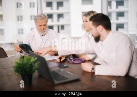 Team of three doctors discuss X-ray of patient in consulting room of hospital Stock Photo
