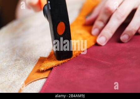 A leather craftsman produces leather goods. He taps the hammer. Handmade work. Stock Photo