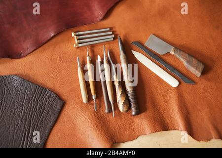 Horizontal high angle shot of various craftwork tools and pieces of leather material of different colours lying on table Stock Photo