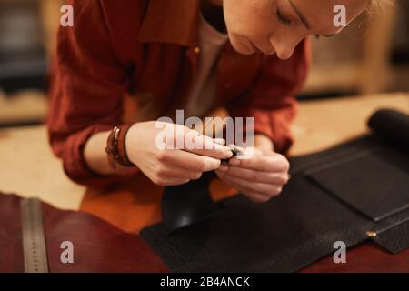Horizontal shot of young female artisan creating something using leather materials of different colours Stock Photo
