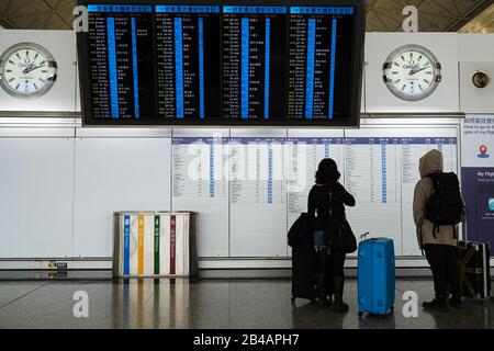 Hong Kong, China. 06th Mar, 2020. Travellers look at the flight schedule information board at Hong Kong International Airport.As the Coronavirus (Covid-19) continues to spread all over the world, many countries have tighten up travel restrictions. Credit: SOPA Images Limited/Alamy Live News Stock Photo