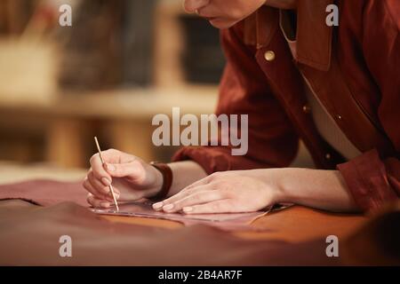 Horizontal close up shot of young female artisan with beautiful hands cutting out piece of brown leather Stock Photo
