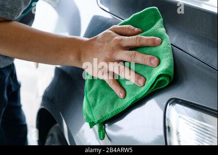 Man cleaning car with green microfiber cloth on car hood Stock Photo