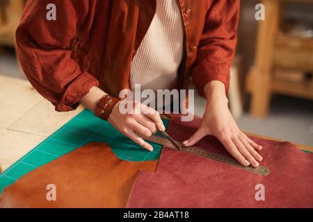 Horizontal high angle close up shot of unrecognizable female artisan cutting leather material Stock Photo