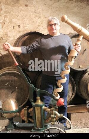 France, Jura, Chateau Chalon, winegrower Jean Pierre Salvadori holding a giant corkscrew in his cellar in front of oak barrels with Macvin du Jura (white wine) Stock Photo