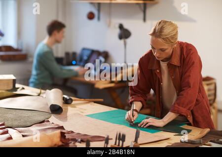 Horizontal shot of young woman on foreground and unrecognizable young man on background doing their job in craft workshop Stock Photo
