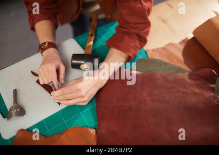 Horizontal from above shot of unrecognizable female artisan using leater punching tool on small detail Stock Photo