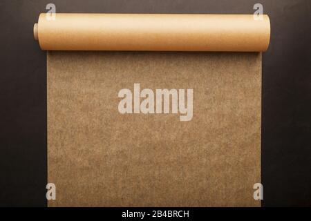 A roll of unfolded brown parchment paper, for baking food in on a dark background, top view. Papyrus Stock Photo