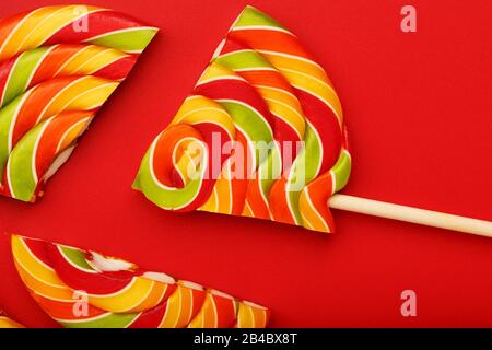 A large multi-colored Lollipop split into pieces, on a scarlet background. Minimal concept, Confectionery product and Goodies Stock Photo