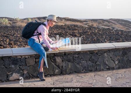 Travel and independence people concept with blonde beautiful adult woman planning the trip with paper map and backpack on his back - outdoor wild desert in background Stock Photo