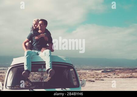 Travel people concept with young couple of man and woman sitting on the roof of old vintage van - love and relationship for travelers - beautiful landscape background Stock Photo
