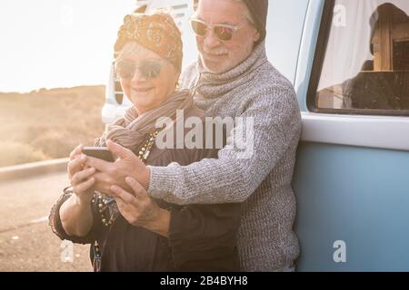 Happy cheerful retired lifestyle old youth people looking together a modern phone in outdoor travel leisure activity concept - hippy coloured happy style - vintage van in background Stock Photo