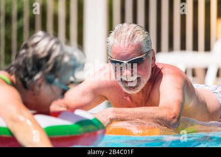Cheerful happy smiling people senior man enjoying the summer swimming pool in couple retired nice lifestyle - white hair and summer holiday vacation or relax leisure activity Stock Photo
