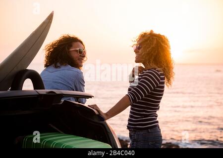 Beautiful people couple of friends curly lady enjoying travel together and have fun with the sunset on the ocean - summer holiday vacation concept with happy females and car and luggages Stock Photo