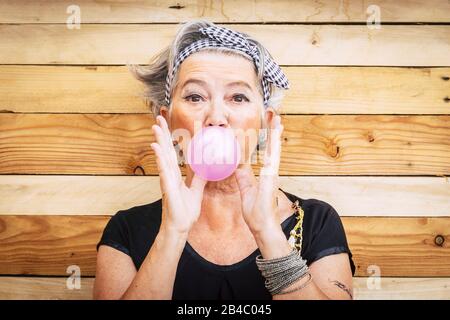 Funny and alternative old people caucasian beautiful woman with pink bubble chewing gum - portrait of youth active senior lady having fun - no limit age lifestyle concept Stock Photo