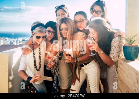 Happy and cheerful people young beautiful women look a picture on a smartphone having fun - outdoor celebration concept for friends together - blue sea in background and smiles Stock Photo