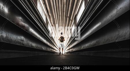 Lonely traveler man with backpack wolking in a steel urban tunnel - city tourism in rare scenic places concept - exploring outdoor and indoor - people enjoying adventure and alternative travel