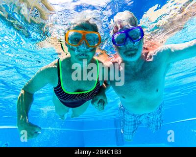 Adult people senior couple have fun swimmin in the pool underwater with coloured funny diving masks - dive concept and active retired man and woman enjoying the lifestyle - blue water and caucasian adults Stock Photo
