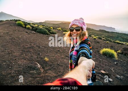 Beautiful cheerful adult young woman smile and holding man hand during outdoor leisure activity trekking at the mountain - travel couple concept for active people - freedom holiday vacation in the nature