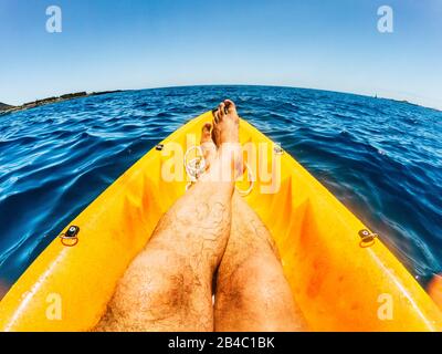 Total lifestyle relax and desconnection concept with men legs in point of view on yellow kayak with blue ocean water around - tourism and travel holiday destination - outdoor leisure activity people Stock Photo