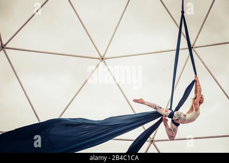 Sport healthy lifestyle people alternative dance in the sky balanced with cords and fabrique - clear white sky in background and steel structure - circus training for fitness babe Stock Photo