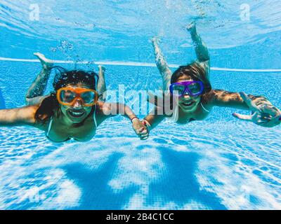 Underwater funny couple of women people having fun together in friendship - summer holiday vacation concept - travel and enjoy lifestyle in ohtel resort clear water swimming pool - cheerful ladies Stock Photo