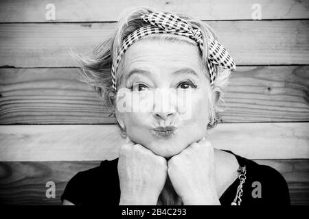 senior and mature woman with makeup is looking at the camera - funny moment with a wood table at the background - cheerful old lady go crazy and nice looking at you Stock Photo