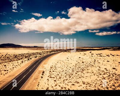 Long black asphalt road in the middle of the desert with nature and outdoors around - concept of travel and adventure in alternative beautiful senic place - aerial view